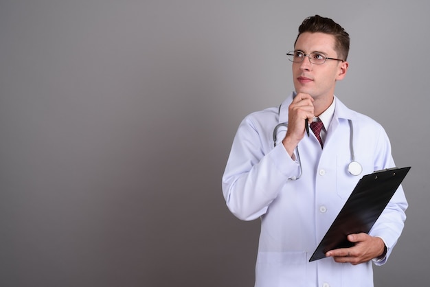 young handsome man doctor wearing eyeglasses on gray