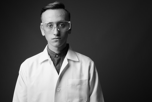 young handsome man doctor wearing protective glasses against gray wall. black and white