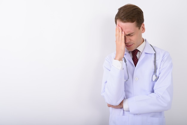 Young handsome man doctor on white wall