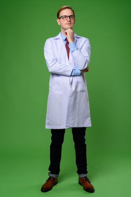 Young handsome man doctor with blond hair against green backgrou