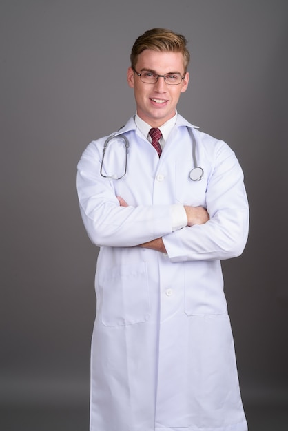 Young handsome man doctor with blond hair on grey wall