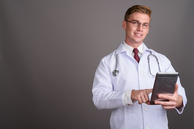 Young handsome man doctor with blond hair on grey wall