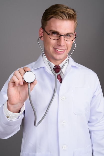 Young handsome man doctor with blond hair on grey wall