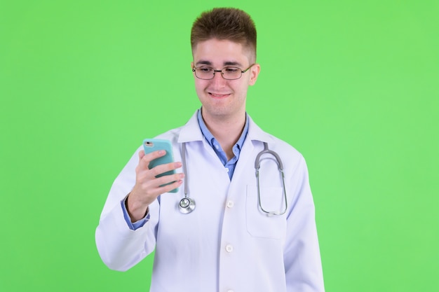 young handsome man doctor with eyeglasses against chroma key with green wall