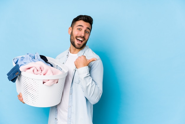 Photo young handsome man doing laundry isolated points with thumb finger away, laughing and carefree.