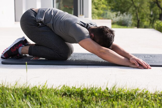 Giovane bell'uomo che fa esercizi di yoga mattutini davanti alla sua villa di lusso