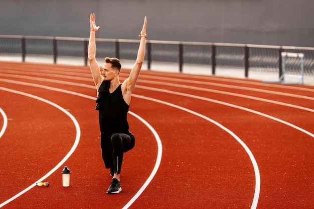 Young handsome man doing stretching before running in the stadium wearing black sport clothes at sum