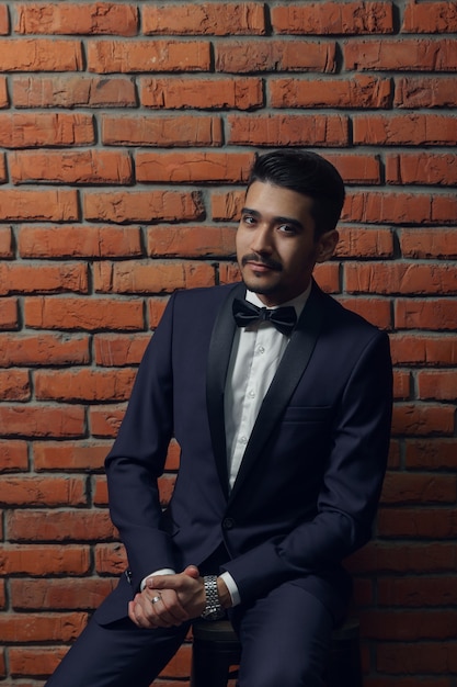 Young handsome man in elegant suit with butterfly on the brick wall background.