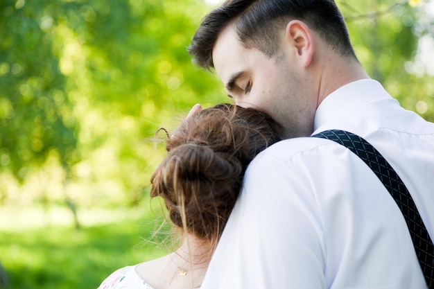 Фото Молодой красивый мужчина обнимает и нежно целует свою невесту в летнем зеленом парке вид сзади на свидание невеста с невестой влюбленная пара
