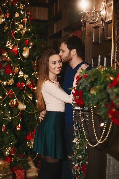 Foto giovane uomo bello che abbraccia e bacia splendida donna modello all'interno decorato per natale