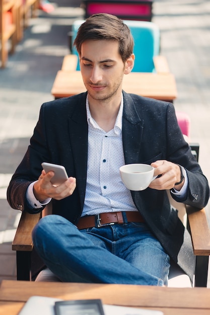 若いハンサムな男がテキストメッセージしながらコーヒーを楽しむ