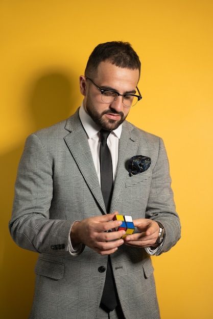 Young handsome man in eye glasses wearing a suite solving a Pocket Cube 2x2x2 rotatable puzzle in