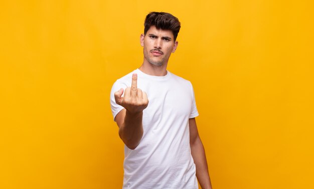 Young handsome man feeling angry, annoyed, rebellious and aggressive, flipping the middle finger, fighting back