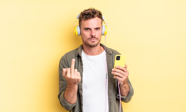 Young handsome man feeling angry, annoyed, rebellious and aggressive headphones and smartphone concept