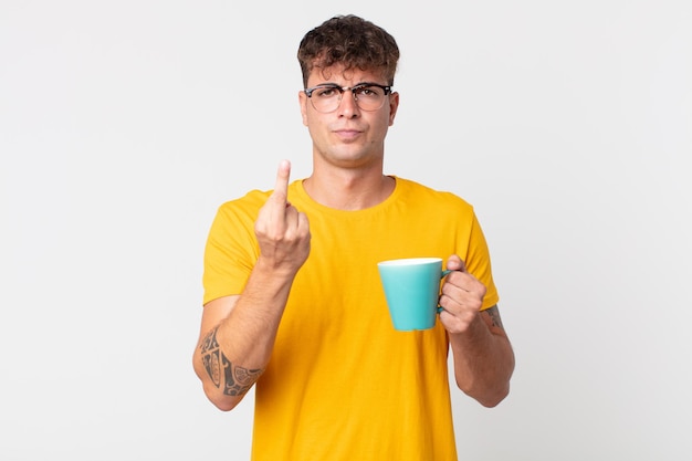 Young handsome man feeling angry, annoyed, rebellious and aggressive and holding a coffe cup