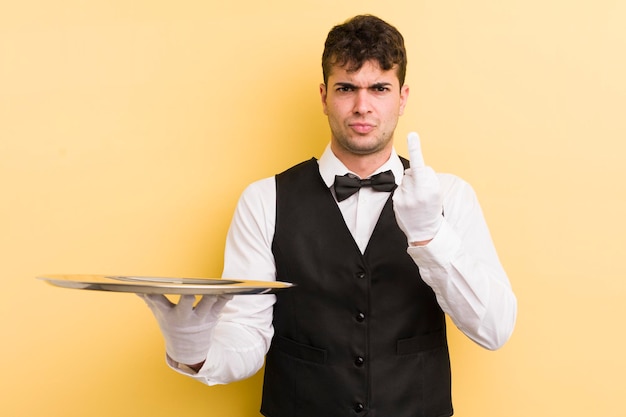 Young handsome man feeling angry annoyed rebellious and aggressive waiter and tray concept