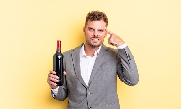 young handsome man feeling confused and puzzled, showing you are insane. bottle of wine concept