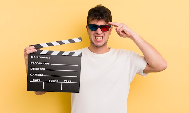 Young handsome man feeling confused and puzzled showing you are insane cinema clapper concept