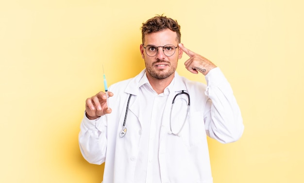 Young handsome man feeling confused and puzzled, showing you are insane. physician syringe concept