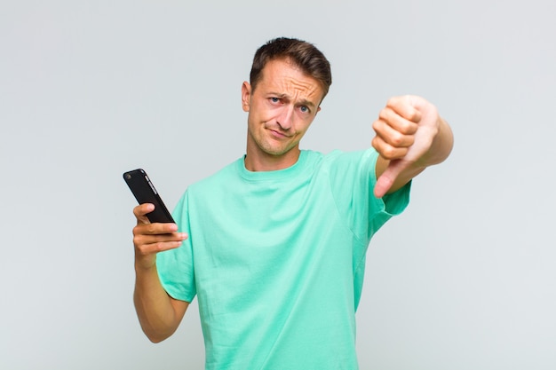 Young handsome man feeling cross, angry, annoyed, disappointed or displeased, showing thumbs down with a serious look