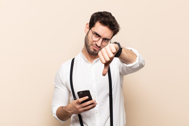 Young handsome man feeling cross, angry, annoyed, disappointed or displeased, showing thumbs down with a serious look