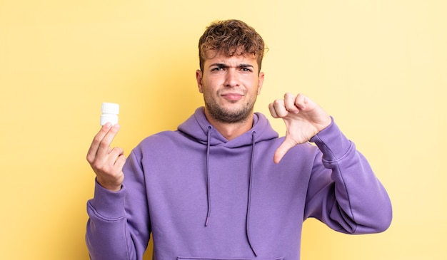 Young handsome man feeling cross,showing thumbs down. pills bottle concept