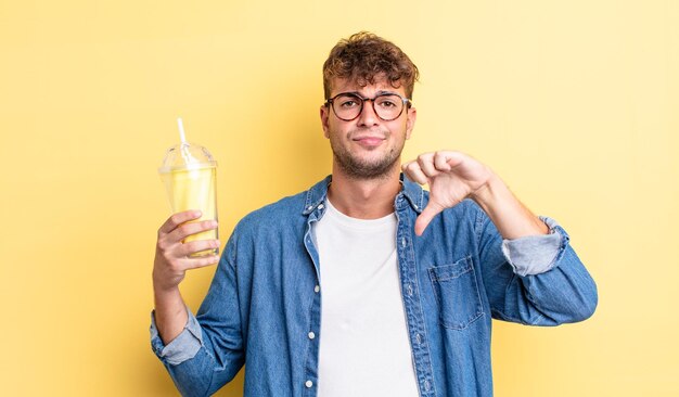 Young handsome man feeling crossshowing thumbs down milkshake concept