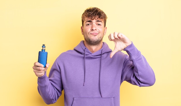 Young handsome man feeling crossshowing thumbs down vaporizer concept