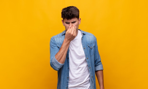 Young handsome man feeling disgusted, holding nose to avoid smelling a foul and unpleasant stench