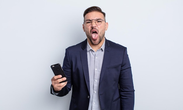 Young handsome man feeling disgusted and irritated and tongue out business and smartphone concept