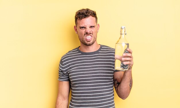 Young handsome man feeling disgusted and irritated and tongue out. water concept