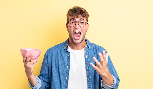 Young handsome man feeling extremely shocked and surprised. empty bowl concept