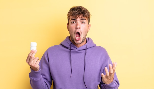 Young handsome man feeling extremely shocked and surprised. pills bottle concept