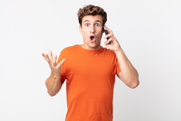 Young handsome man feeling extremely shocked and surprised and talking with a smart phone