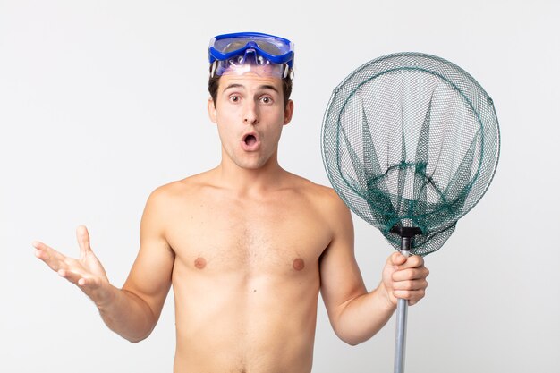 Young handsome man feeling extremely shocked and surprised with goggles and a fishing net