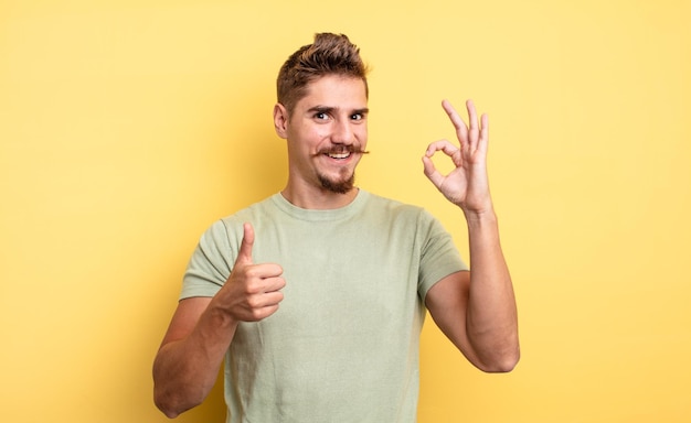 Young handsome man feeling happy, amazed, satisfied and surprised, showing okay and thumbs up gestures, smiling. strange moustache concept