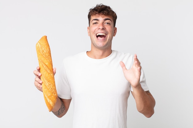 젊고 잘생긴 남자는 믿을 수 없는 일에 행복하고 놀라며 빵 바게트를 들고 있다