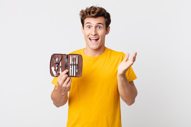 Young handsome man feeling happy and astonished at something unbelievable and holding a nails tools case