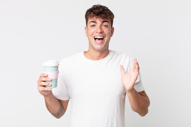 Young handsome man feeling happy and astonished at something unbelievable and holding a take away coffee