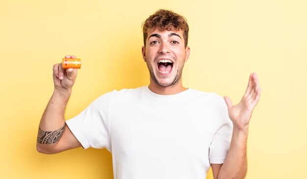 Young handsome man feeling happy and astonished at something unbelievable with a battery