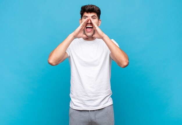 Young handsome man feeling happy, excited and positive, giving a big shout out with hands next to mouth, calling out