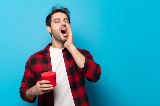 Young handsome man feeling happy, excited and positive, giving a big shout out with hands next to mouth, calling out