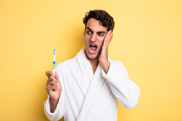 Young handsome man feeling happy, excited and surprised. bathrobe and toothbrush concept