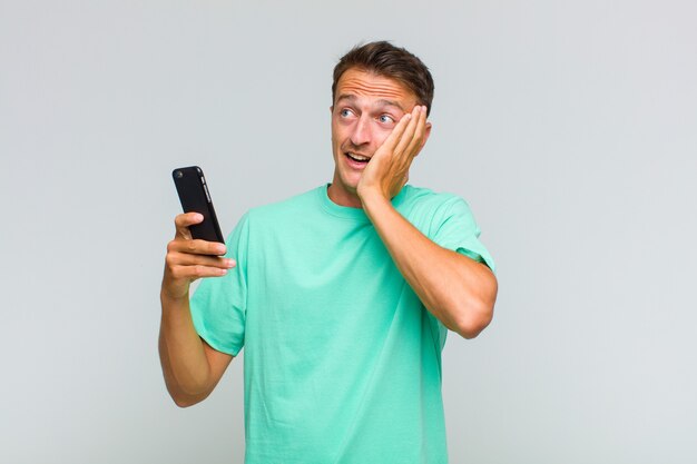 Young handsome man feeling happy, excited and surprised, looking to the side with both hands on face