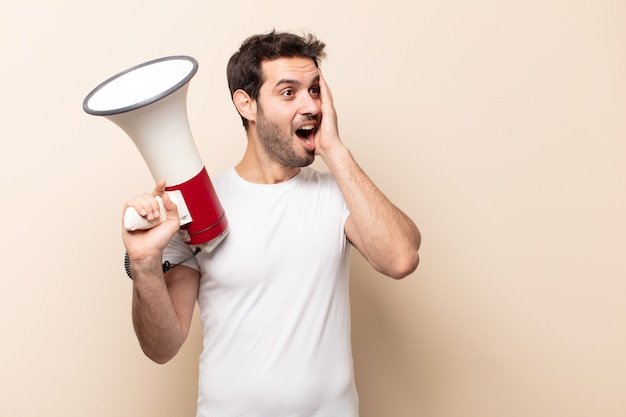 young handsome man feeling happy, excited and surprised, looking to the side with both hands on face