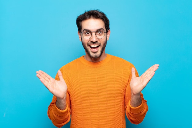 Young handsome man feeling happy, excited, surprised or shocked, smiling and astonished at something unbelievable