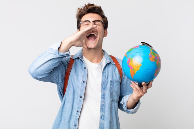 写真 幸せを感じて、口の横に手で大きな叫びを与える若いハンサムな男。世界の地球地図を持っている学生