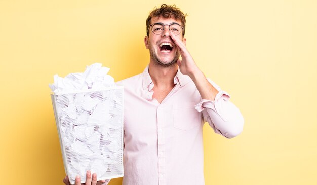 Young handsome man feeling happy,giving a big shout out with hands next to mouth. paper balls trash concept