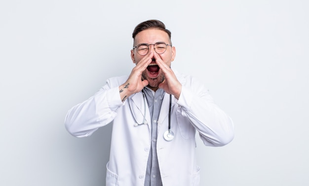 Giovane uomo bello sentirsi felice, dando un grande grido con le mani vicino alla bocca. concetto di medico