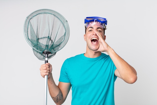 Young handsome man feeling happy,giving a big shout out with hands next to mouth with goggles and fishing net